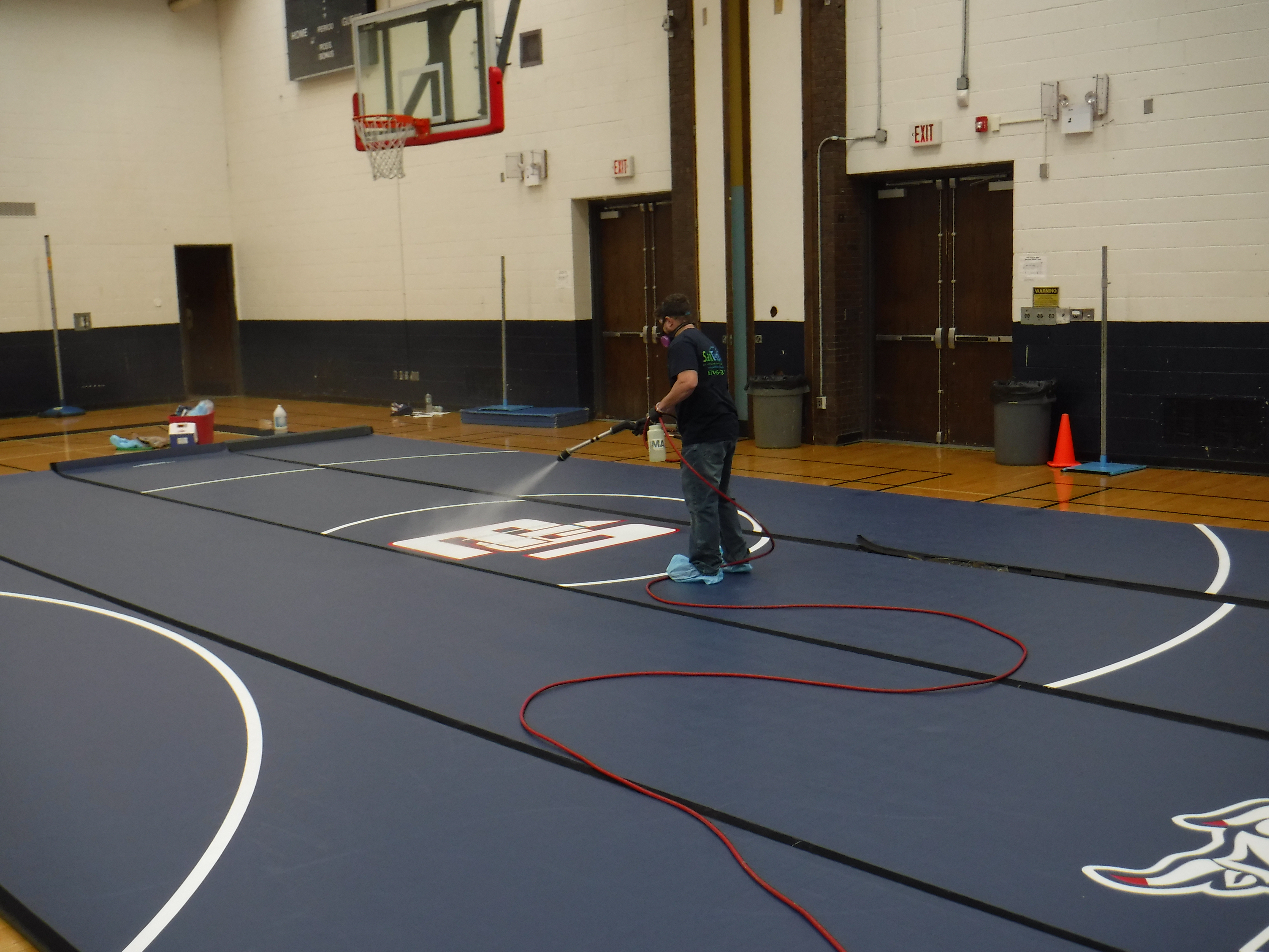 SaniTech technician applying antimicrobial treatment to wrestling mats in school gymnasium